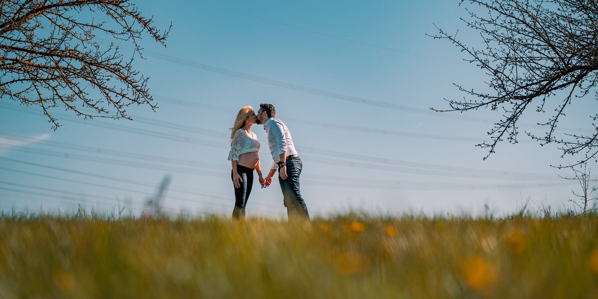 Babybauch-Shooting Osthessen – Schwangeres Paar küsst sich auf einer Frühjahrswiese