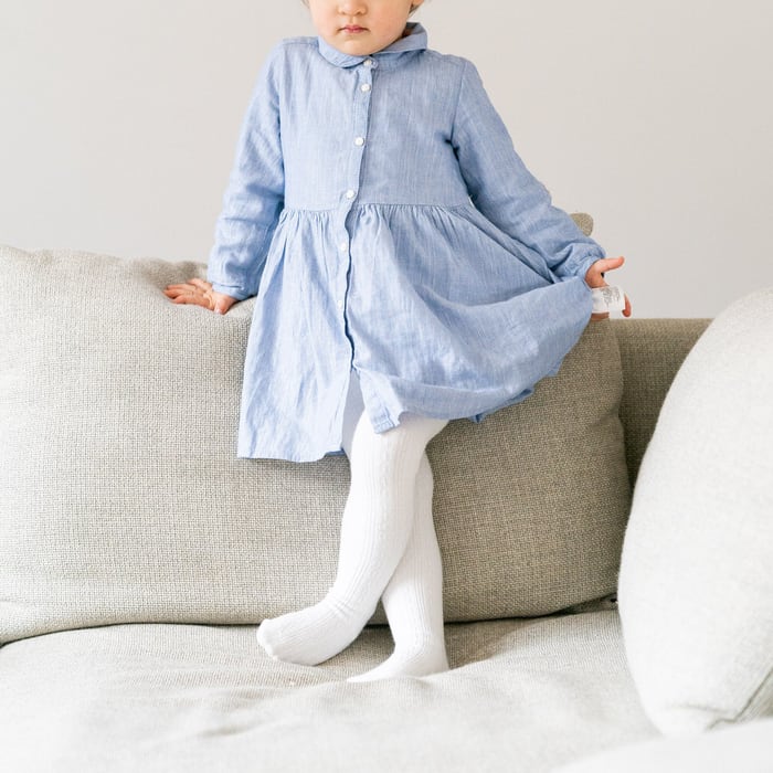 Kinderfotografie Zuhause – Kleines Mädchen im hellblauen Kleid steht auf dem Sofa