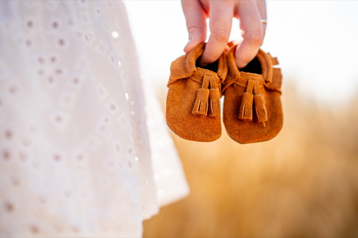 Neugeborenen-Shooting – winzige Babyschuhe werden in der Hand der Mutter gehalten, goldener Hintergrund