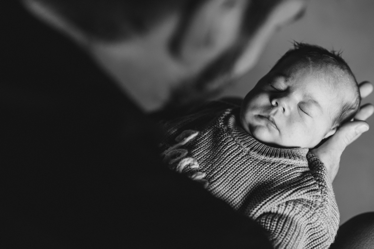 Neugeborenen-Fotoshooting – Vater hält schlafendes Neugeborenes liebevoll in den Armen, emotionales Schwarzweißfoto