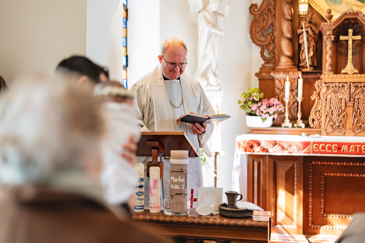Taufe Fotografie – Priester liest in der Kirche, festlich geschmückter Altarbereich mit Kerzen und Blumen