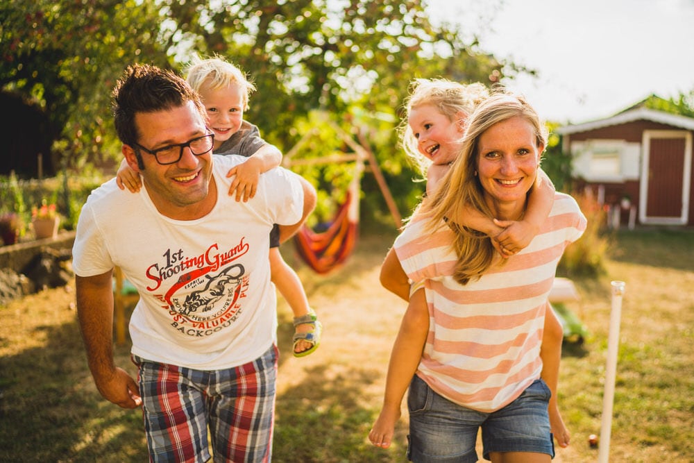 Familienshooting im Garten – Eltern tragen Kinder auf dem Rücken