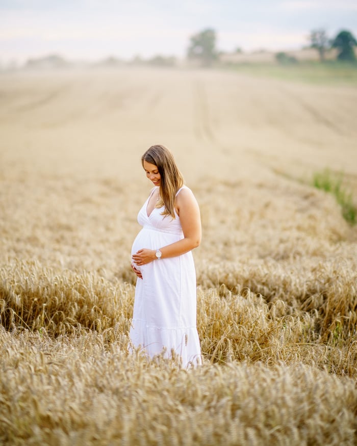 Babybauch-Shooting Fulda – Schwangere Frau im weißen Kleid im goldenen Weizenfeld bei Sonnenuntergang